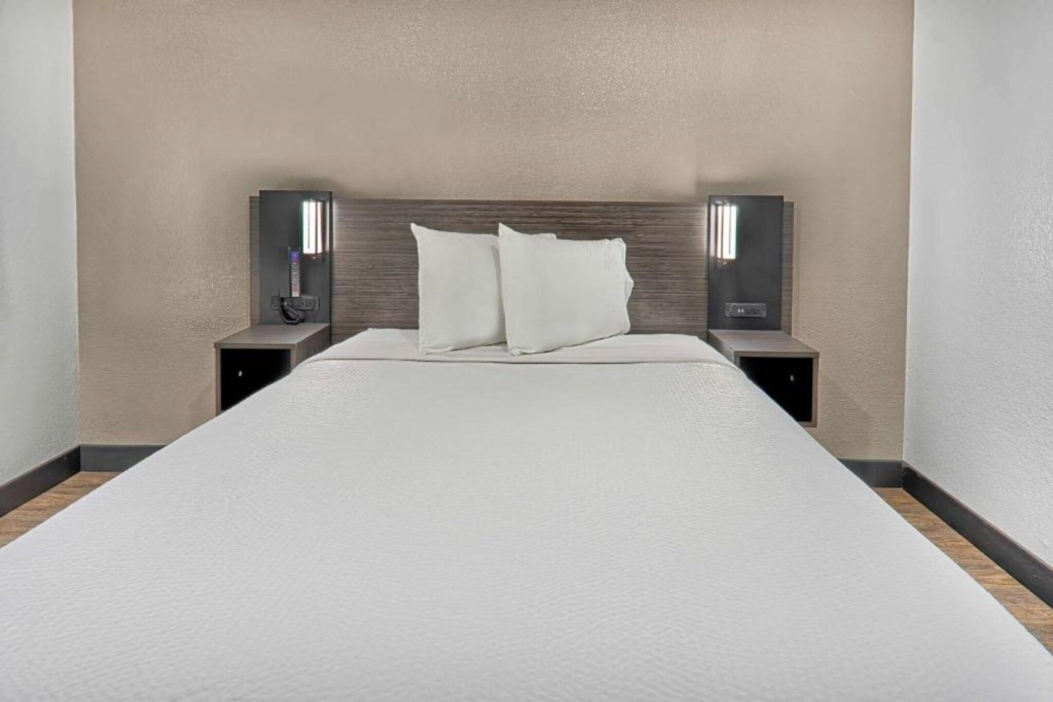 A hotel room with a large bed, two bedside tables, and two wall-mounted lamps.
