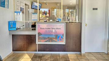 A reception desk with a sign promoting a mobile app, a computer monitor, and informational posters on the wall.
