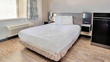A hotel room with a bed, bedside tables, a heater, a wardrobe, and a window with curtains.