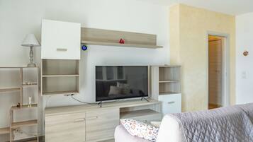 Ein modernes Schlafzimmer mit Fernseher an einer Holzeinrichtung, einem Nachttisch mit Lampe und einem Bett mit gemustertem Überwurf.