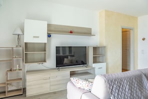Un dormitorio moderno con un televisor montado en un mueble de madera, una mesita de noche con una lámpara y una cama con un edredón estampado.