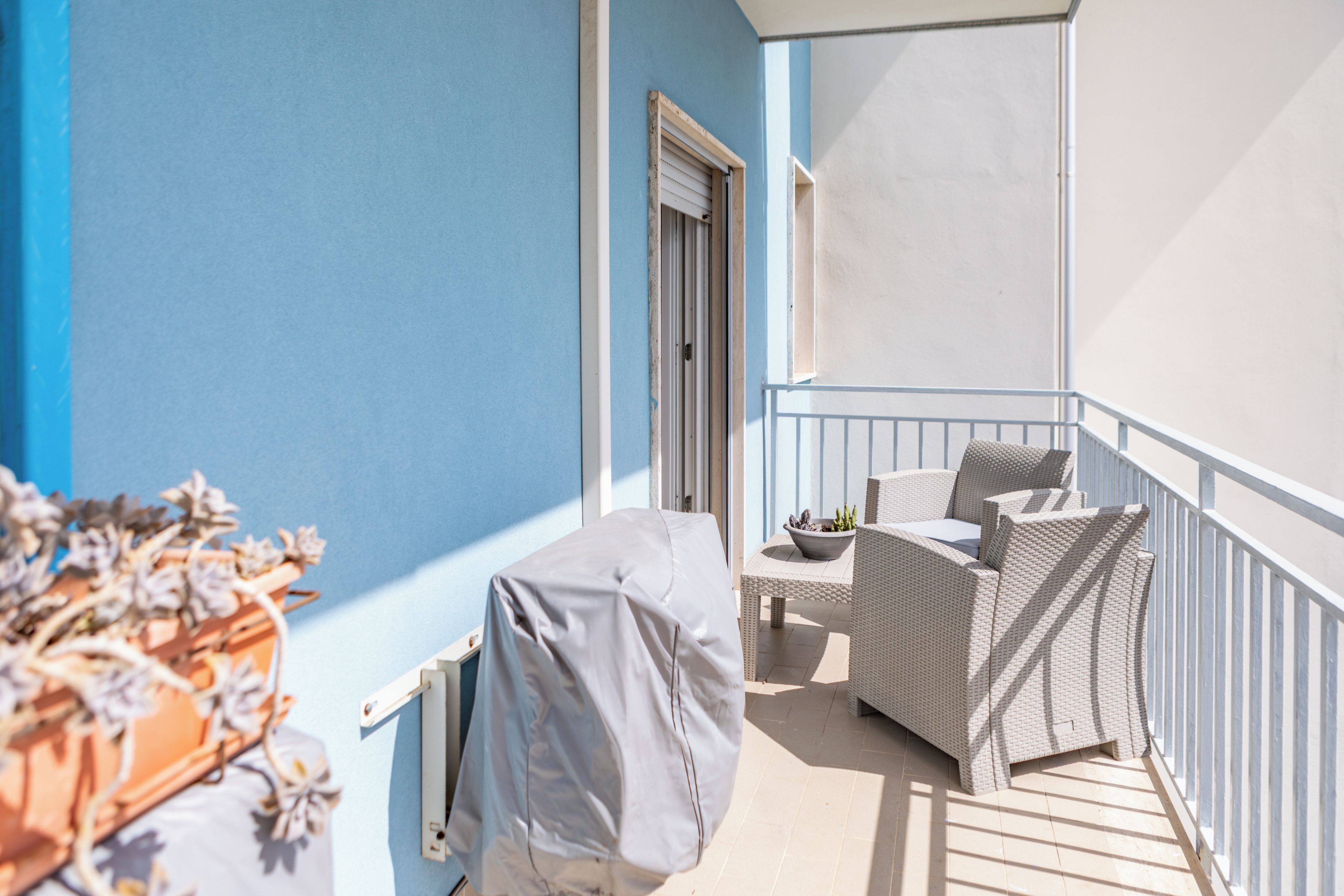 Een balkon met een overdekte tafel, een rieten stoel en een bloempot.