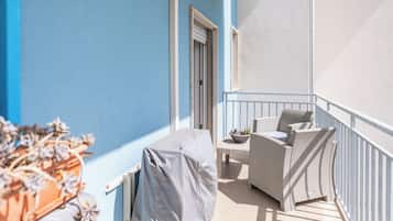 Een balkon met een overdekte tafel, een rieten stoel en een bloempot.