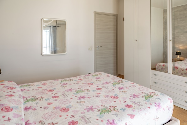 A bedroom with a bed, a wardrobe, a mirror, and a nightstand with a lamp.