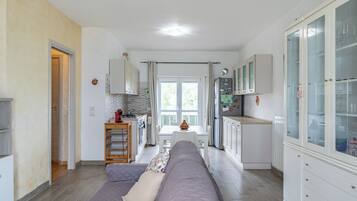 Eine moderne Küche mit weißen Schränken, ein Essbereich mit Tisch und Stühlen sowie eine Wohnbereich mit Sofa und Kissen.