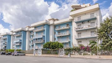 A multi-story residential building with balconies, a gated entrance, and a clear sky.
