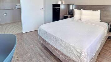 Een hotelkamer met een groot bed, nachtkastje, stoel en een kledingkast.