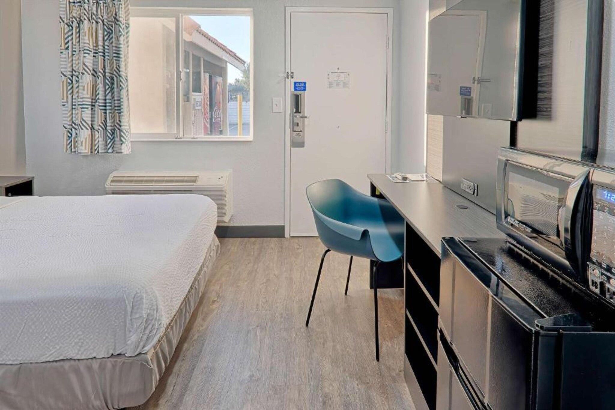 A hotel room with a bed, a desk, a chair, a television, and a window with curtains.
