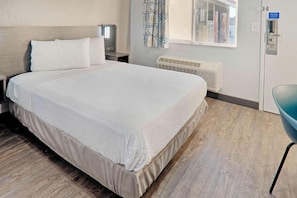 Habitación de hotel con cama, mesita de noche, calentador de pared y ventana con cortinas.