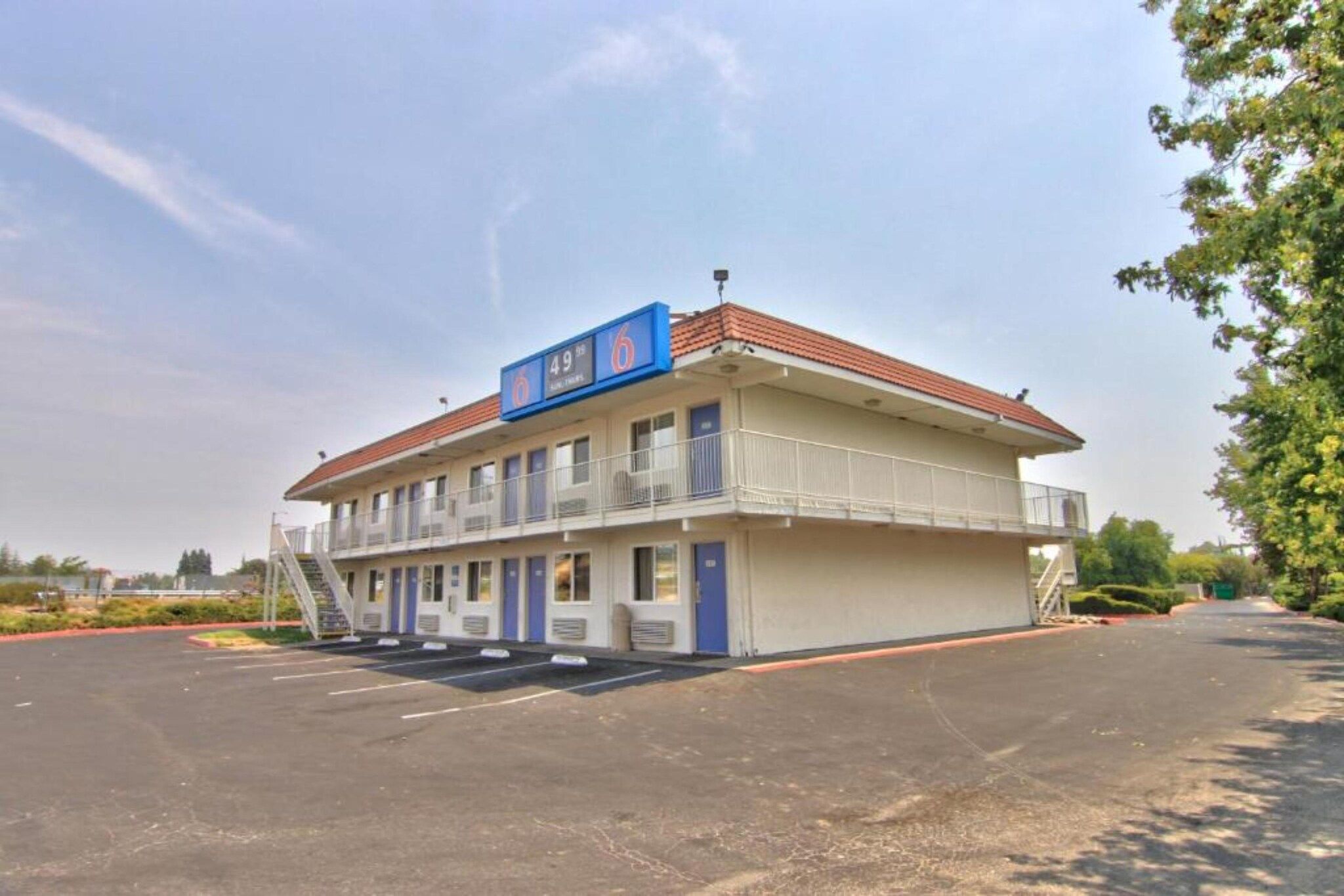 A two-story building with a flat roof, a blue sign on the top, and a parking lot in front.