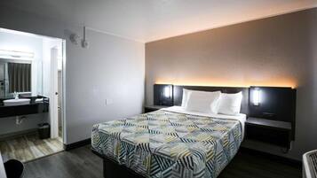 A hotel room with a bed, bedside tables, a nightstand, a mirror, and a bathroom with a sink and toilet.