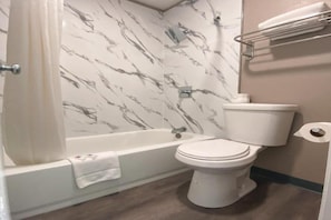 A bathroom with a bathtub, toilet, and marble-patterned walls.