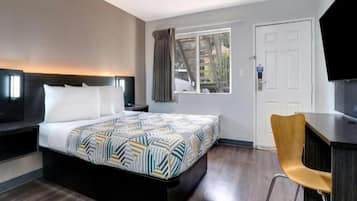 A hotel room with a bed, a desk, a chair, a television, and a window with curtains.