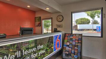 A motel lobby with a reception desk, a clock, and a view of the outside.