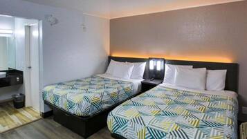 A hotel room with two beds, a small bedside table, a mirror, and a door.