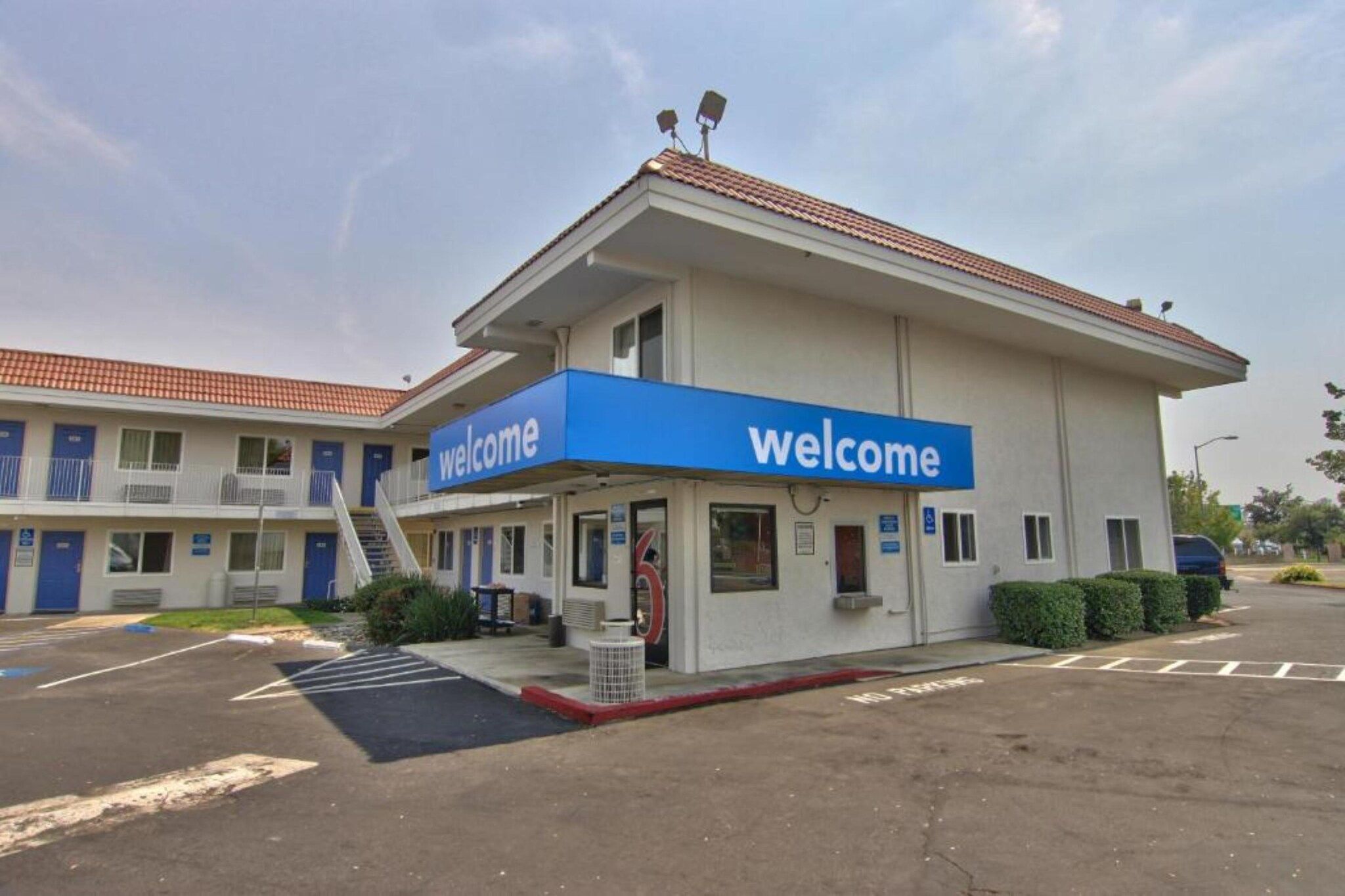 A building with a blue 'welcome' sign, a parking lot, and a clear sky.