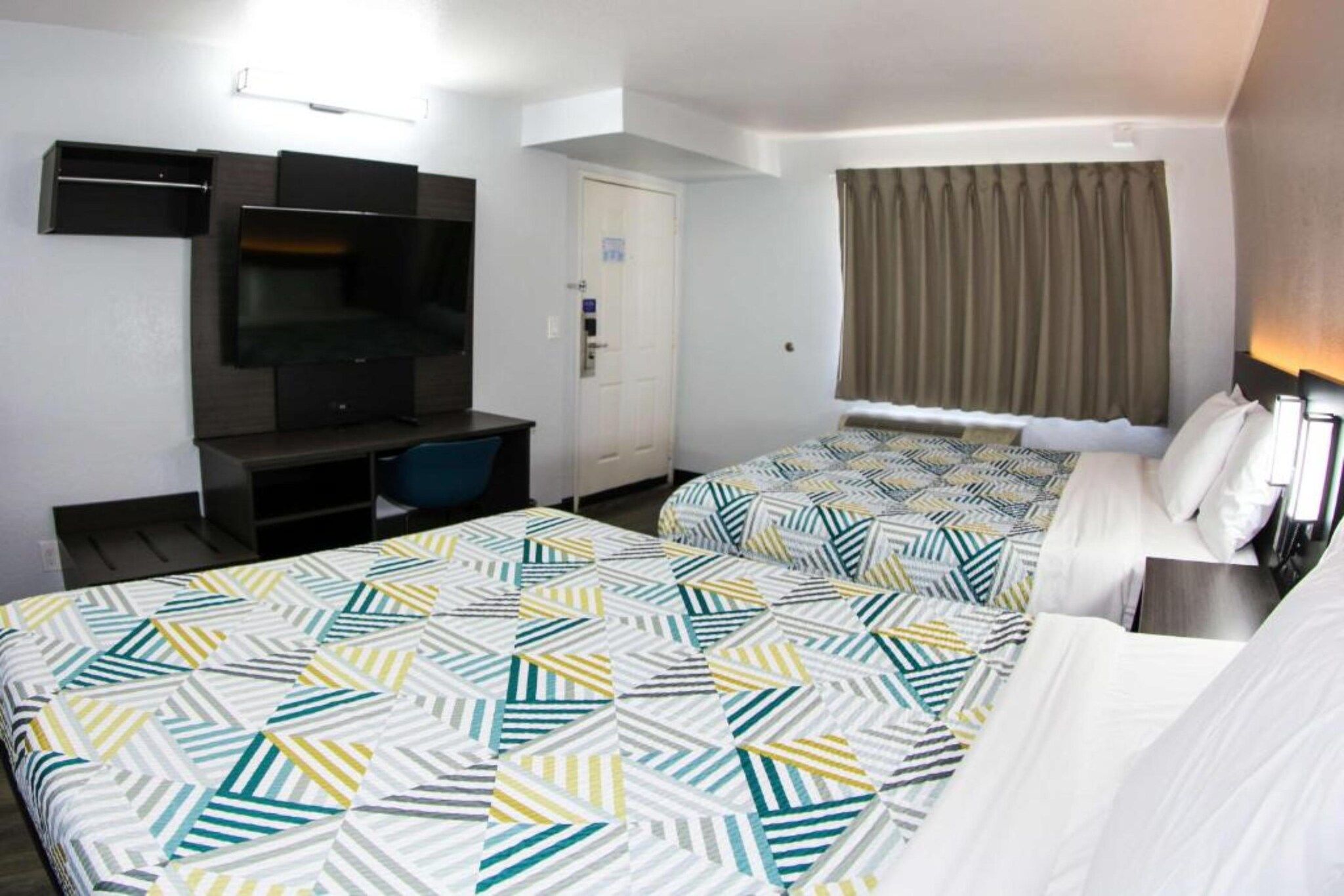 A hotel room with two beds, a desk, a television, and a window with curtains.