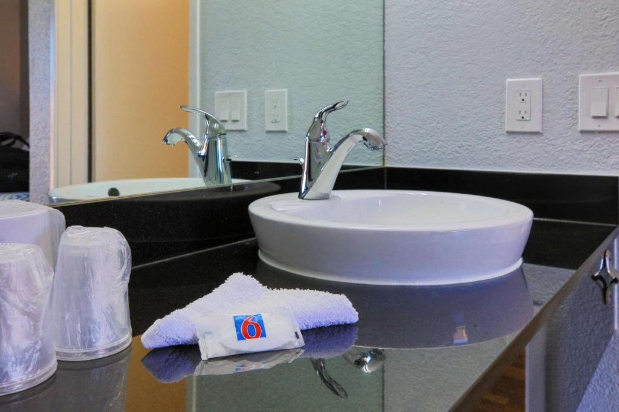 A hotel bathroom with a round sink, a mirror, and a towel on the counter.