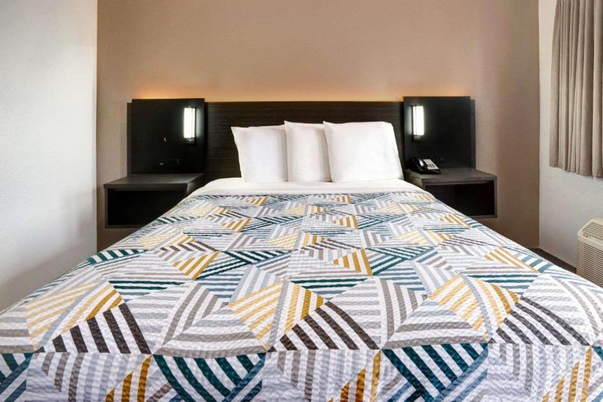 A hotel room with a bed, two bedside tables, and a nightstand with a lamp.