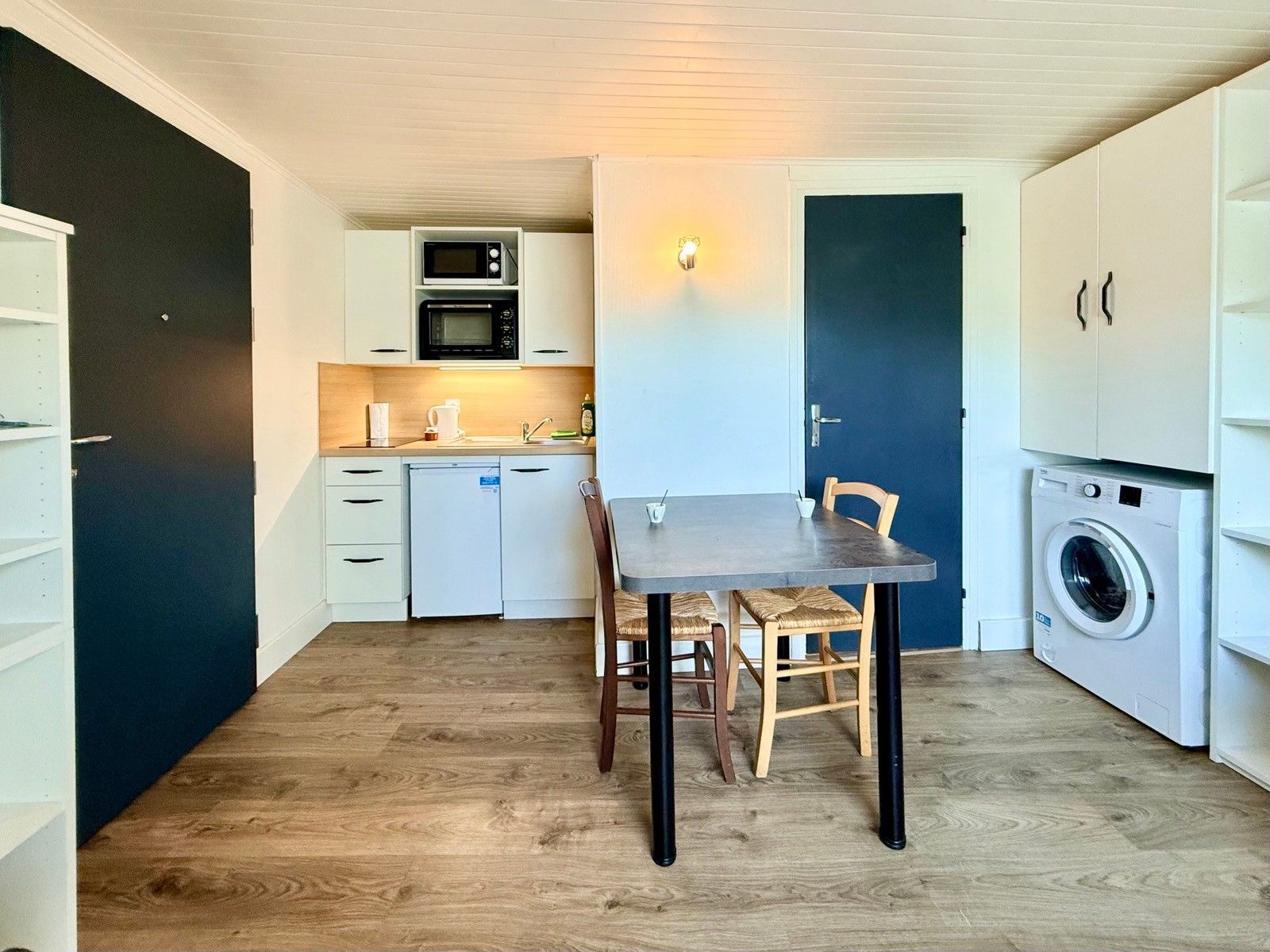 A compact kitchen with a dining table, chairs, a microwave, oven, and a washing machine.