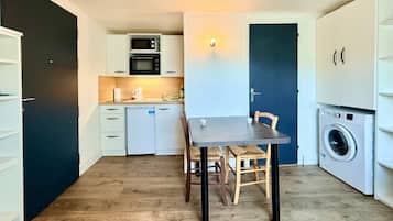 A compact kitchen with a dining table, chairs, a microwave, oven, and a washing machine.