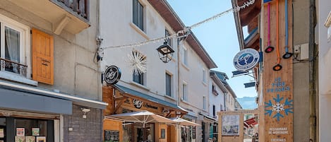 Una calle estrecha con edificios de madera, mesas al aire libre y letreros de restaurantes.