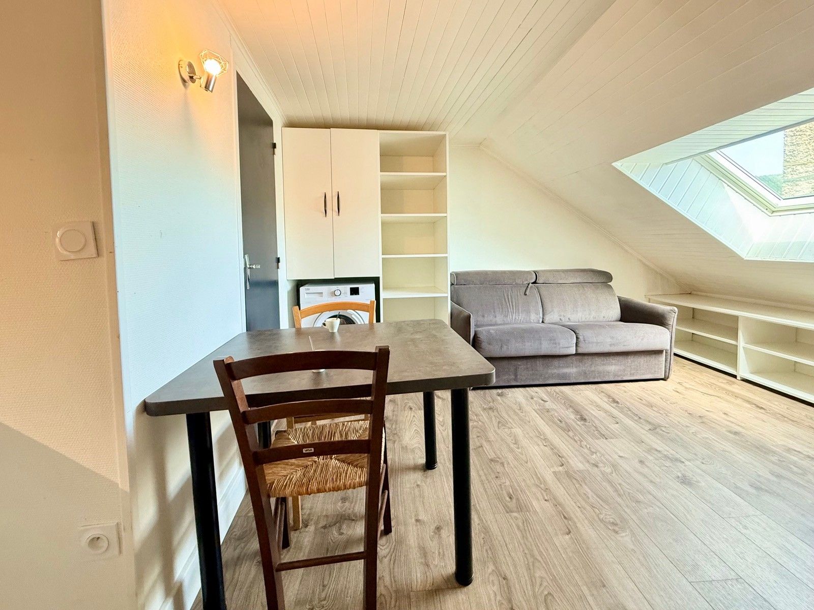 A compact living space with a dining table, a grey sofa, and a skylight.