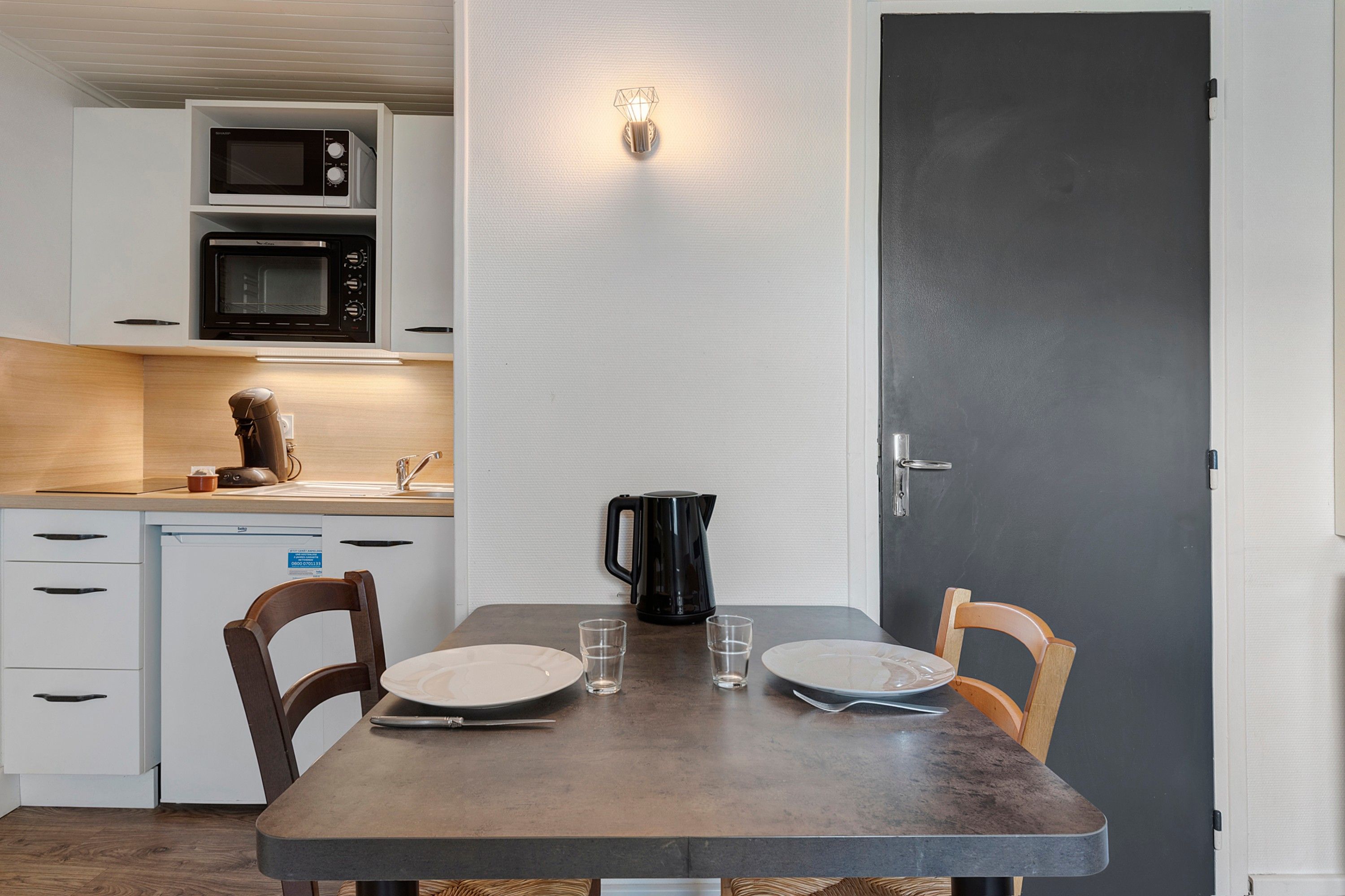 A compact kitchen with a microwave, kettle, and a dining table set for two.
