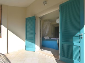 Una habitación con cama, ventana y puerta con contraventanas.