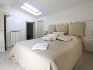 Une chambre à coucher avec un grand lit, une lucarne, un radiateur et une porte donnant sur une autre pièce.