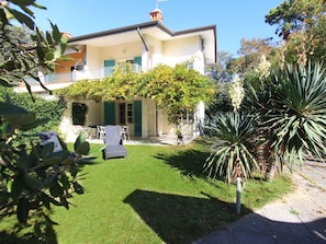 Una casa con porche cubierto, césped y jardín con diversas plantas.