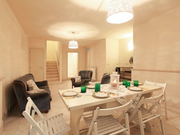 Un coin repas avec une table dressée pour quatre personnes, entourée de chaises, d’un canapé et d’un escalier menant à une autre pièce.