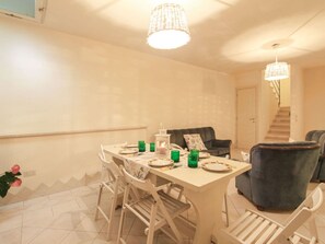 Un comedor con una mesa dispuesta para cuatro, sillas, una vela y un candelabro colgante.