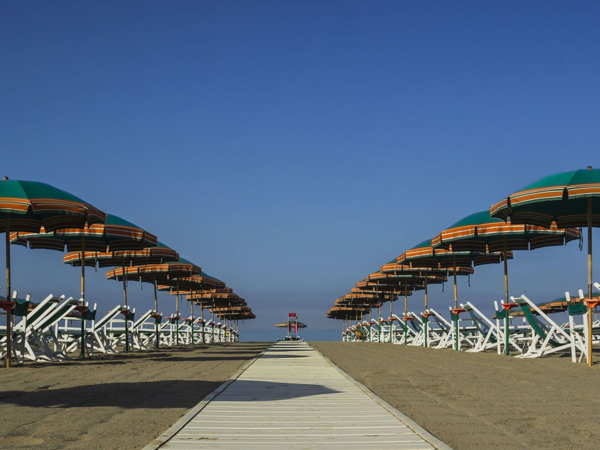 A beach walkway with rows of beach chairs and umbrellas.