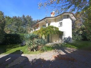 Ein zweistöckiges Haus mit weißer Fassade, einem Balkon und einem Garten mit verschiedenen Pflanzen.