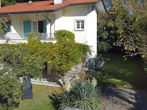 A white building with a red-tiled roof, a balcony with green shutters, and a well-maintained garden with various plants and a pathway. - Beautiful private villa for 6 people with A/C, WIFI, TV and patio (Forte Dei Marmi)