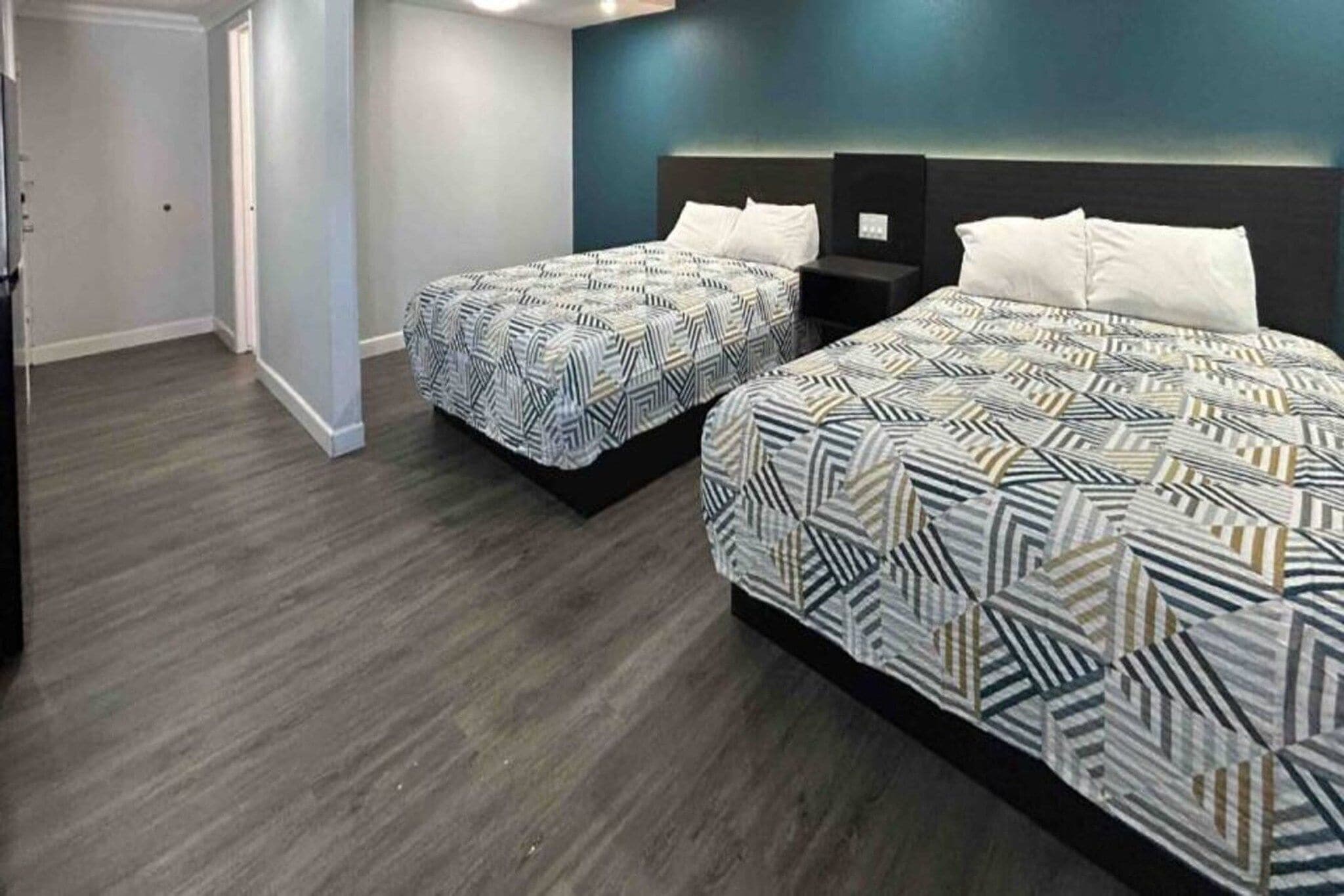 A hotel room with two beds, a dark wood floor, and a blue accent wall.