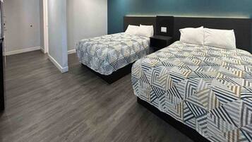 A hotel room with two beds, a dark wood floor, and a blue accent wall.