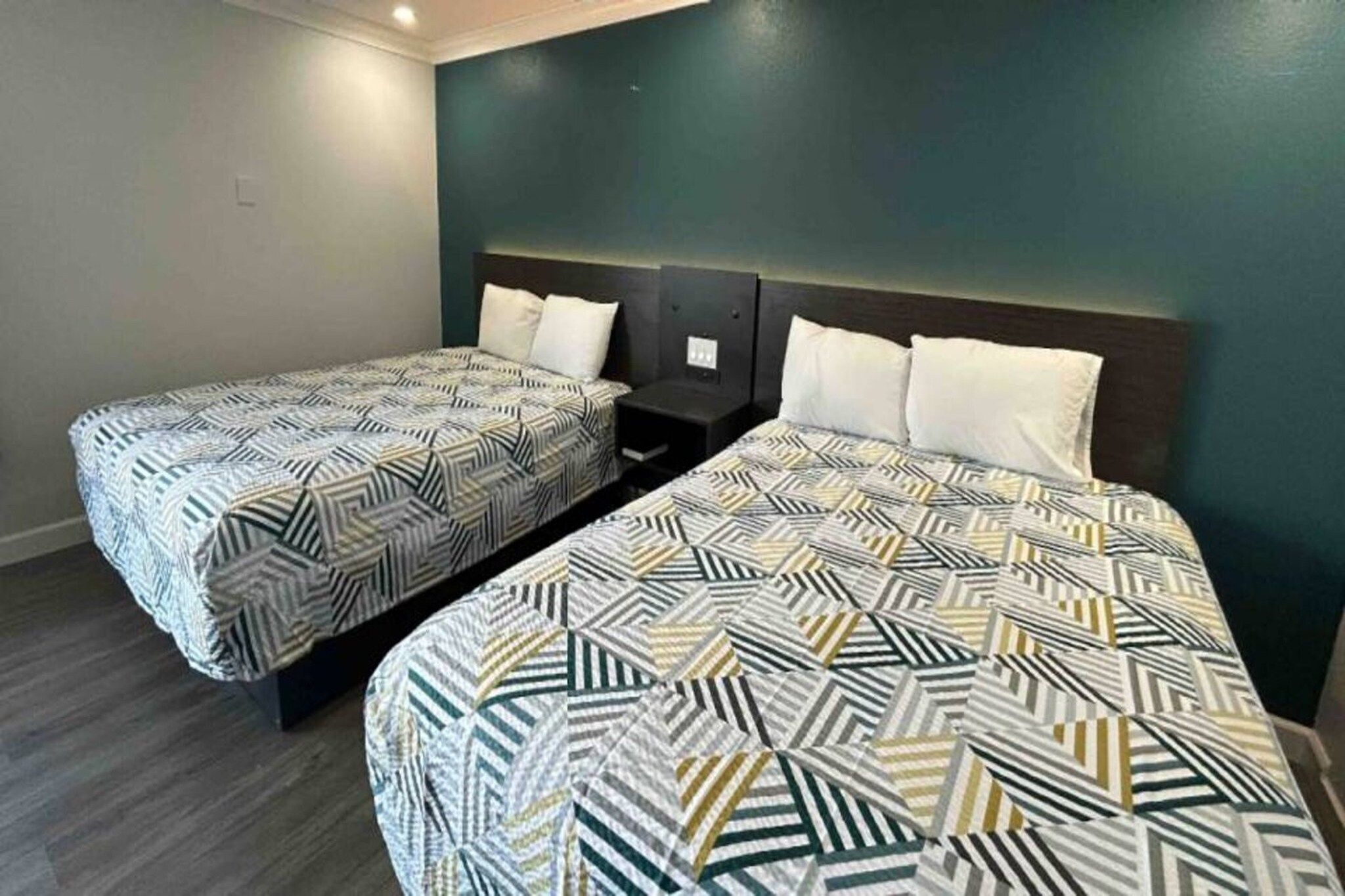 Twin beds with geometric patterned bedding in a room with dark walls and a wooden floor.