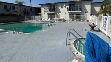A swimming pool with a covered area, a fenced deck, and a building with multiple windows and balconies.