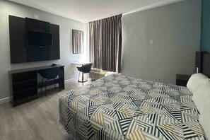 Een hotelkamer met een bed, een bureau, een stoel, een televisie en een raam met gordijnen.