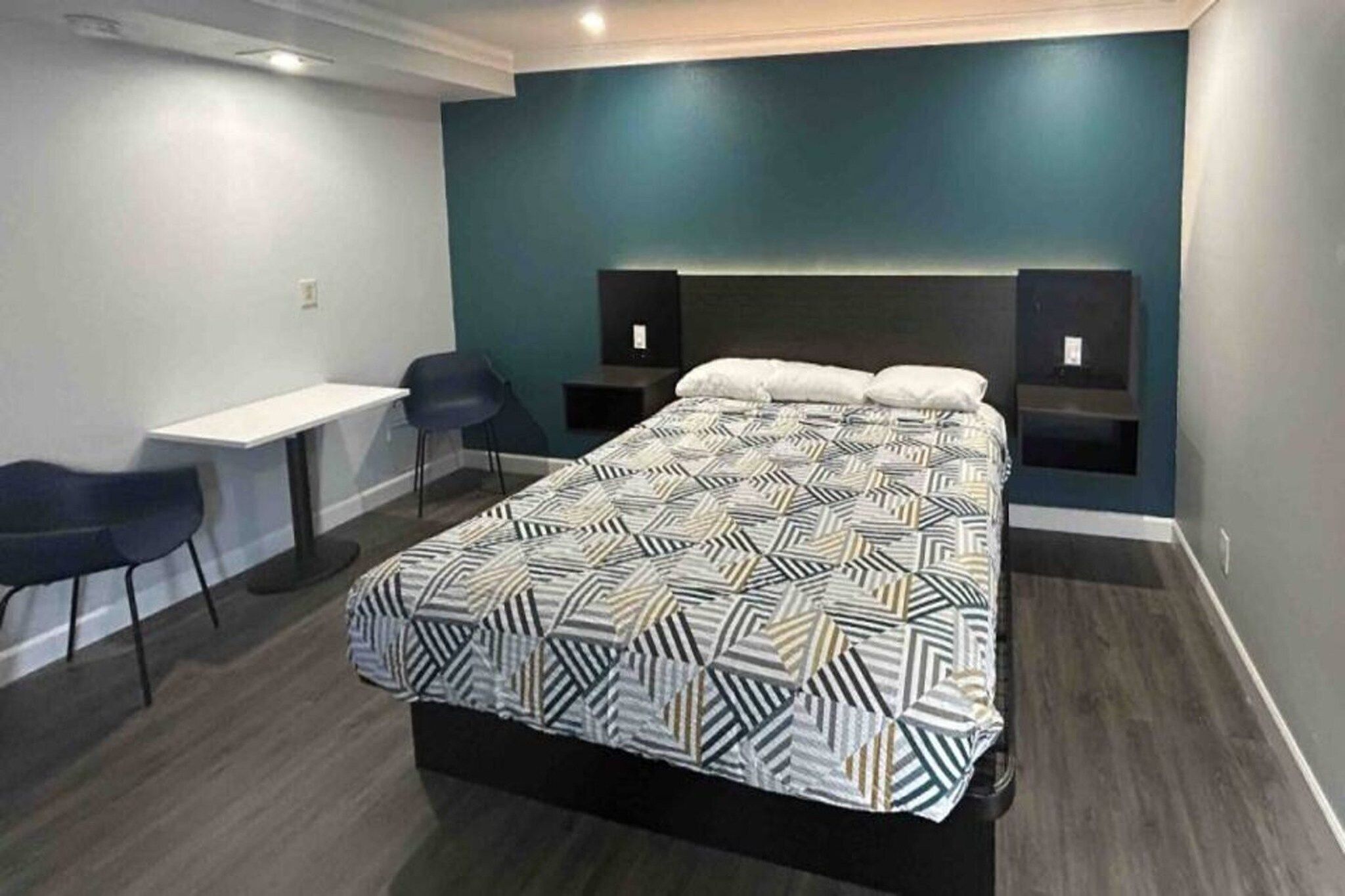 A hotel room with a large bed, a desk, two chairs, and a TV.