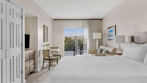 Habitación de hotel con una cama grande, un escritorio con silla, un balcón con vistas y televisión.
