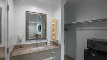 A bathroom with a sink, mirror, towel rack, and a black microwave.