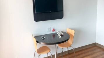 Pieni huone, jossa on pyöreä pöytä, kaksi tuolia, seinälle asennettu taulutelevisio ja pöydällä puhelin.