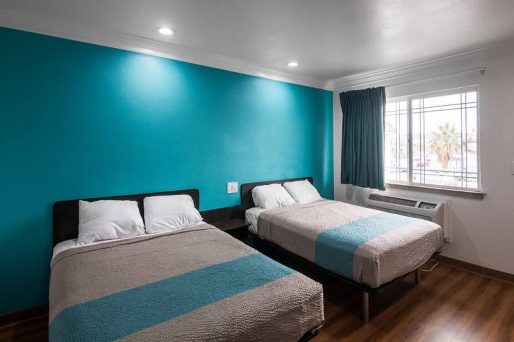 A hotel room with two beds, teal walls, and a window with curtains.