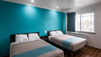 A hotel room with two beds, teal walls, and a window with curtains.
