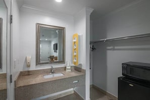 A bathroom with a sink, mirror, towel rack, and a black microwave.