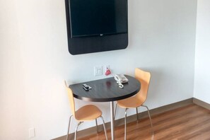 A small room with a round table, two chairs, a flat-screen TV mounted on the wall, and a telephone on the table.