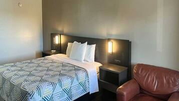 A hotel room with a bed, two bedside tables, a chair, and a wall-mounted light fixture.